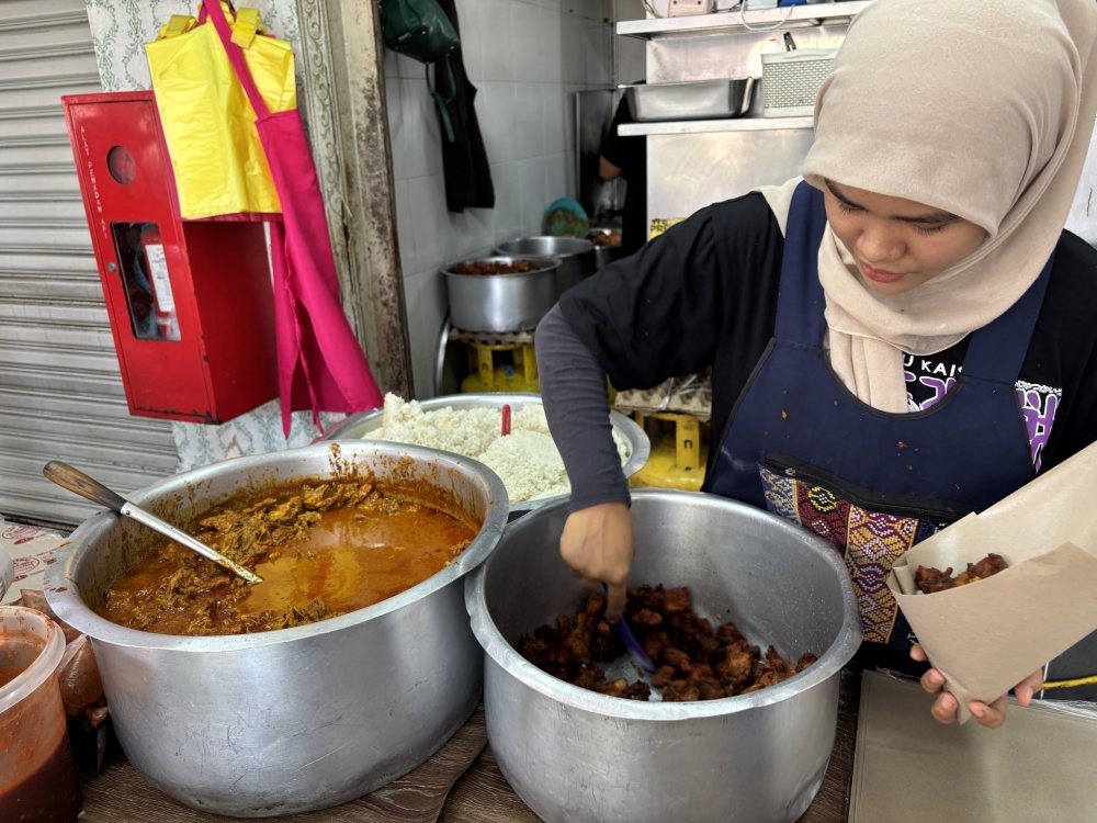 Gerai Kak Meh Nasi Berlauk staff member Halimatum Mahama packs the eatery’s RM6 lunch set comprising rice, curry chicken, fried chicken, ‘sambal belacan’ and curry gravy at the Perak Stadium food court in Ipoh. — Picture by John Bunyan