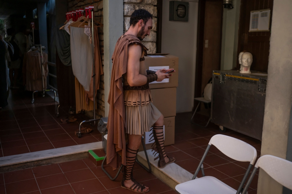 An actor of the opera 'Medea' looks at his smartphone as he stands backstage at the Ancient Greek theatre of former city Epidaurus, in Nea Epidavros on June 18, 2026. With flamboyant costumes reminiscent of those from 1961, and a production reconstructed using notebooks and photographs from the period: 'Medea', the opera that brought Maria Callas her triumph, is being revived at the ancient Greek theatre of Epidaurus. During a one-off, sold-out performance on Saturday evening, the Greek National Opera returns for the first time in 65 years to this 4th-century BC amphitheatre, 200 kilometres from Athens, renowned for its exceptional acoustics. — AFP pic