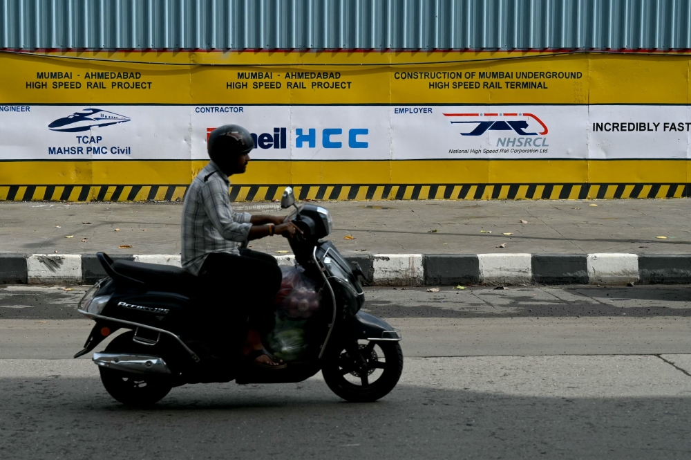 A commuter rides past signs at the construction site of the Ahmedabad-Mumbai high-speed bullet rail project in Mumbai on June 25, 2026. — AFP pic