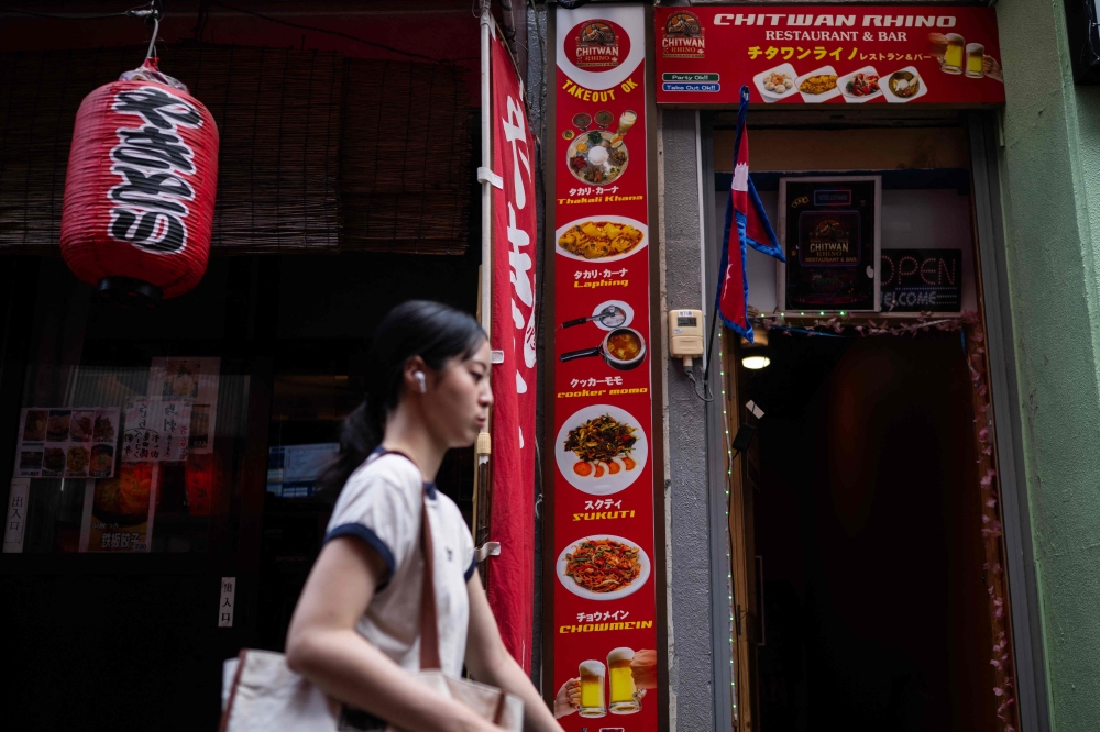 A woman passes a Japanese restaurant and the Chitwan Rhino Restaurant and Bar in the Okubo亡hin area, one stop north of Shinjuku metro, in Tokyo on June 12, 2026, a neighbourhood known for its large immigrant communities, including Korean, South-east Asian and South Asian residents. — AFP pic 