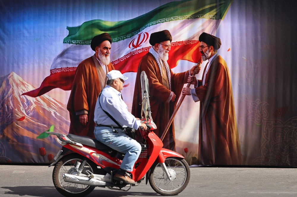 A man rides a scooter past a billboard featuring the images of the late founder of the Islamic Revolution supreme leader Ayatollah Ruhollah Khomeini (left), the Iran’s slain supreme leader Ali Khamenei (centre) and his son, the current supreme leader Mojtaba Khamenei, along the street in Tehran July 3, 2026. — AFP pic