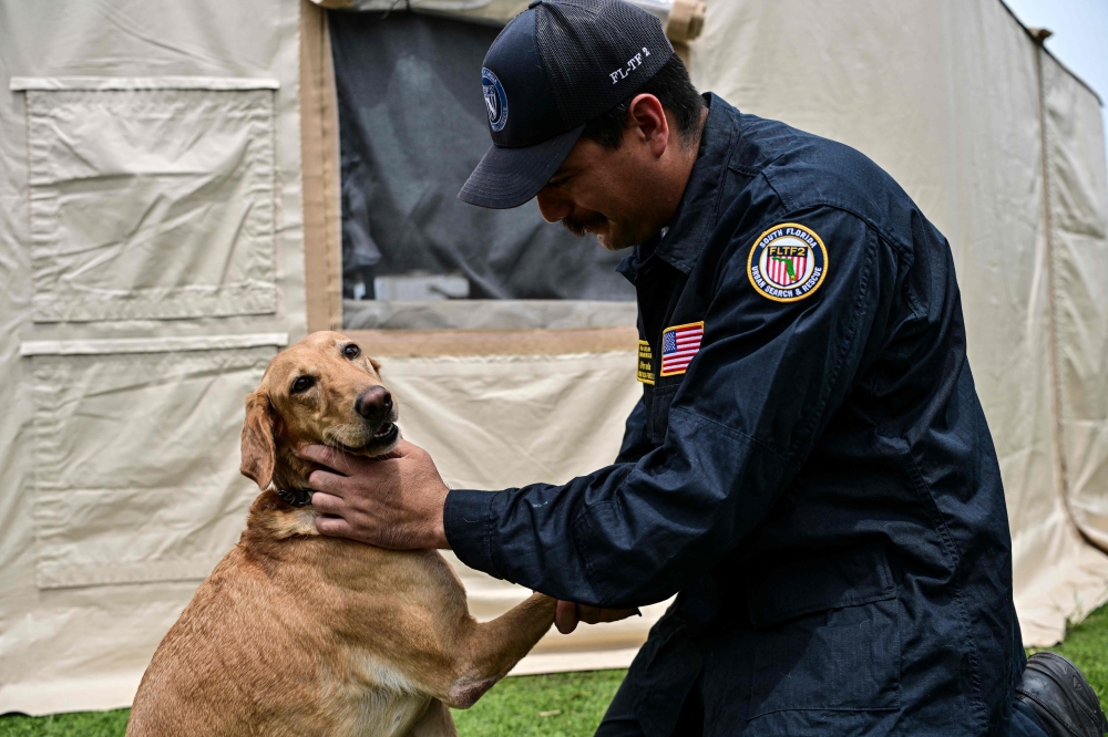 Alexander Parada of the Rescue Florida Task Force 2 team pets his labrador retriever dog Piper, who participated in the rescue works, at a camp in Maiquetia, La Guaira state, Venezuela, on July 4, 2026, ten days after twin earthquakes. — AFP pic
