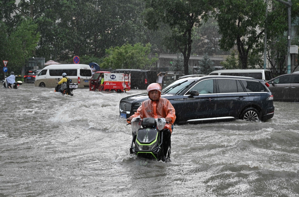 A man on a scooter makes his way along a flooded street in Beijing on July 7, 2026. — AFP pic 