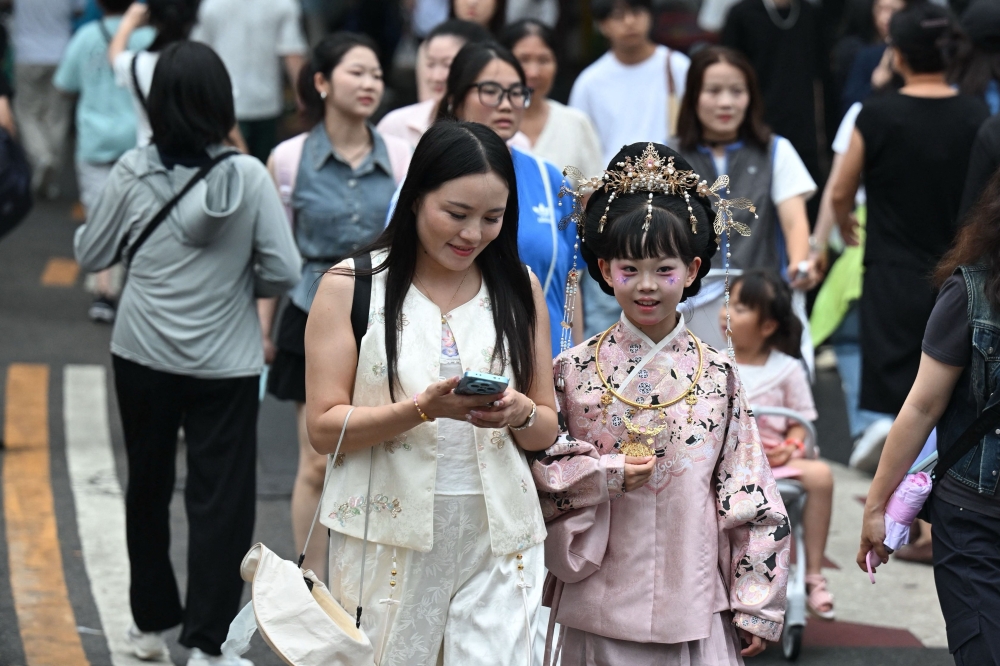 A woman (centre) looks at her phone as people visit the Shichahai scenic area in Beijing on July 10, 2026. — AFP pic