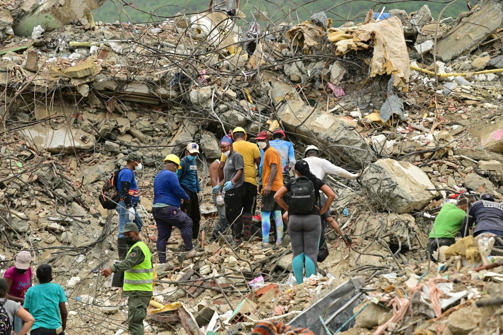 Relatives of missing people and rescue workers search for victims amid the rubble of a collapsed building in Caraballeda. — AFP pic