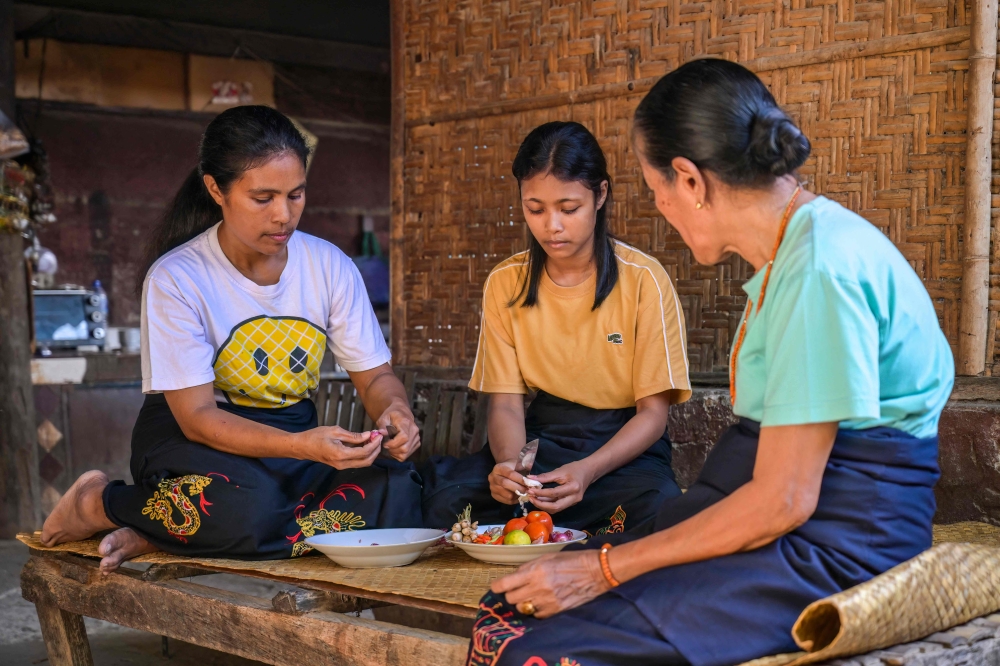 This photo taken on June 24, 2026 Rambu Margaretha (R), a maramba (noblewoman), looking on as two atas (slaves/servants) prepare ingredients for a meal at Kampung Raja Prailiu at Waingapu in East Sumba, East Nusa Tenggara. — AFP pic