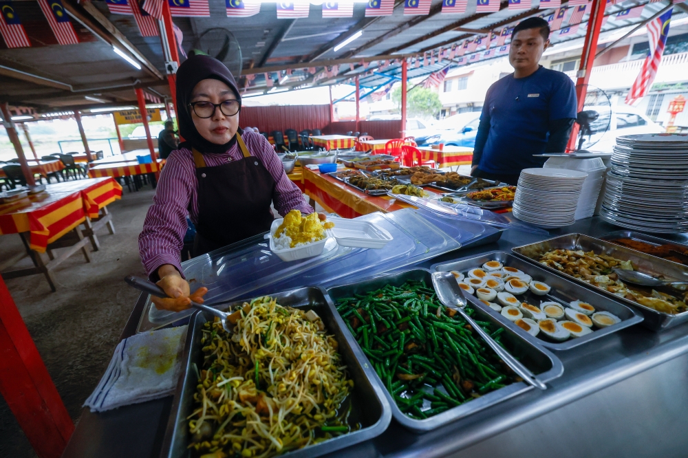 Warung Dayang Salai D’Linggi owner Rozianah Ahmad, 57, serves a customer after preparing her signature smoked ‘baung’ dish in Port Dickson. — Bernama pic