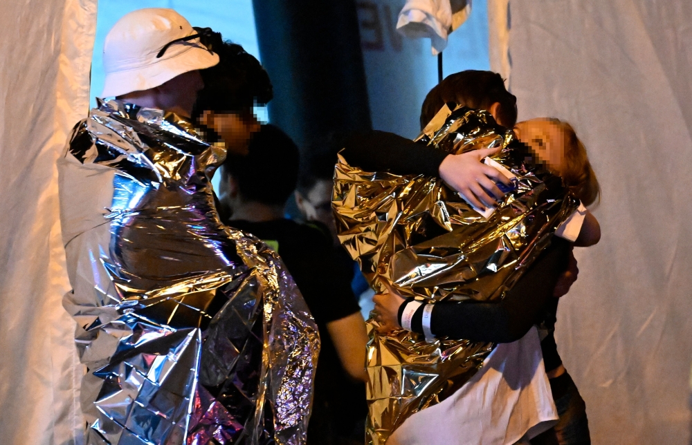 People wrapped in security blankets hug near the scene where one person was killed and around 15 injured after a car is believed to have hit the crowd on the outskirts of the Christopher Street Day parade in Berlin, on July 25, 2026. — AFP pic
