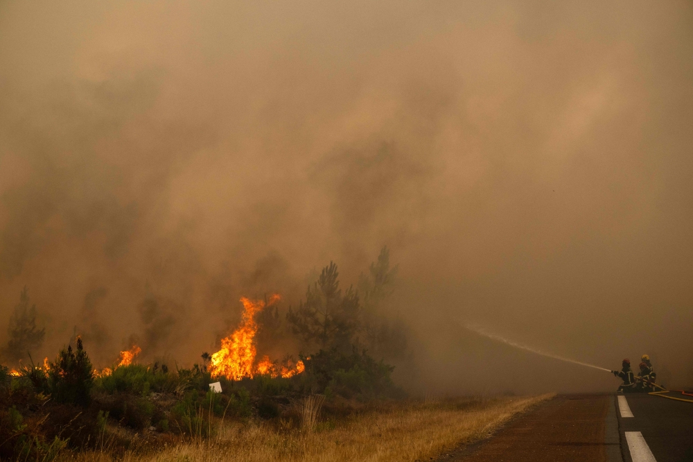 Firefighters spray water along the edge of a forest during a wildfire near the town of Lege-Cap-Ferret, in south-western France on July 25, 2026. — AFP pic