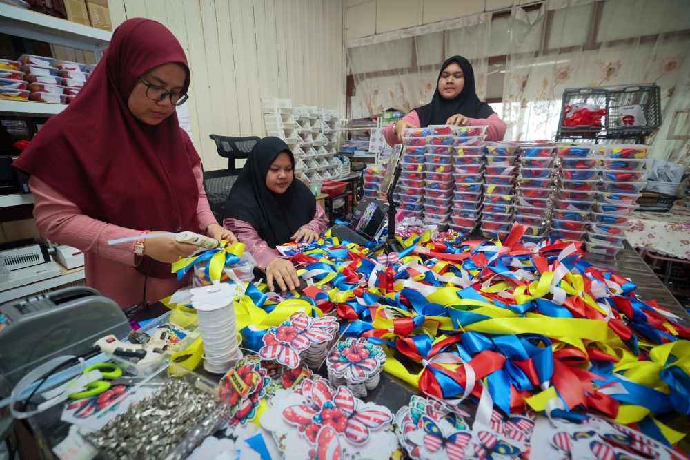 Ridh Leo Craft owner Reedhwah Reef’ah Abdul Rashid (centre), together with her employees Nur Ashirah A’tiah Mohamad Bakhtiar and Wan Asiah Zakaria@Wan Sulaiman, prepare Jalur Gemilang ribbons for online sale in Kampung Paya Senang. — Bernama pic