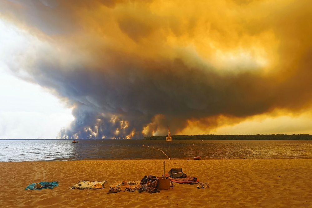 This photograph shows beach towels on the beach of Moutchic in Lacanau, southwestern France on July 24, 2026, as clouds of smoke rise into the sky from a wildfire. — AFP pic