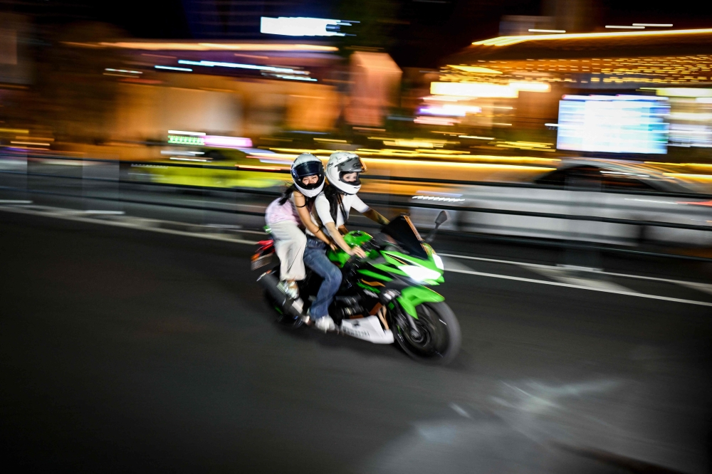 Two women ride a motorcycle along a street in Chongqing July 21, 2026. — AFP pic