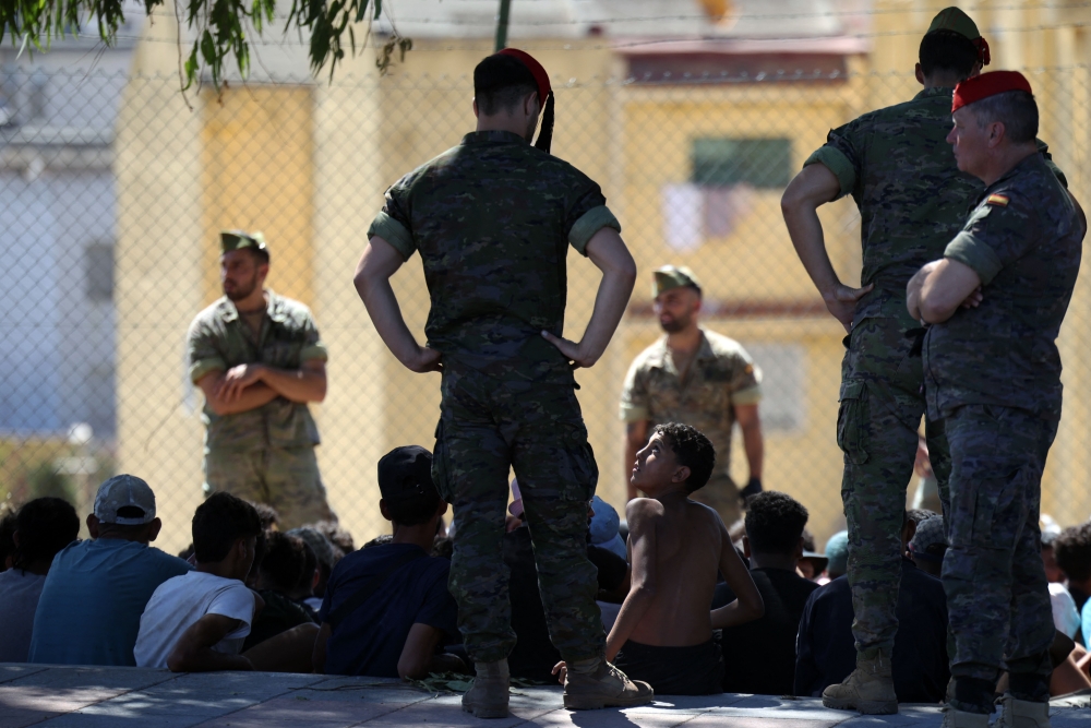 A young migrant looks at a member of the Spanish Army’s ‘Regulares’ infantry force near the border post, prior to escorting them back to Morocco, in the Spanish enclave of Ceuta on August 2, 2026. — AFP pic
