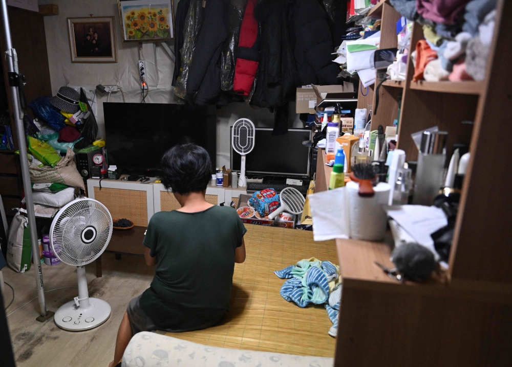 A woman sits in front of a fan inside her one‑room shack in Guryong Village, on the edge of Seoul’s Gangnam district, August 4, 2026. — AFP pic
