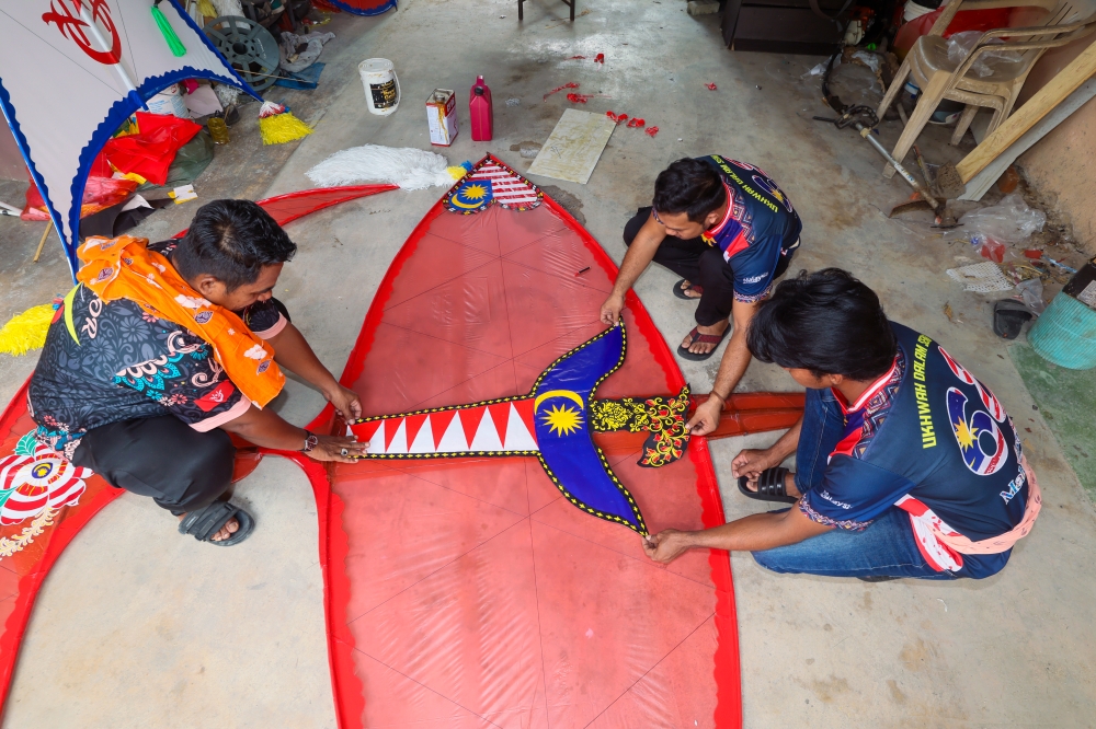 ‘Wau’ maker Mohd Norazizi Mustapha, 45, (left) from Kampung Padang Bongor, Binjai, works on two mega ‘wau’, a ‘wau bulan’ and ‘wau kucing’, for the Merdeka Mega Kite Competition 2026 at Pantai Cherang Laut, Kampung Senok, Bachok, on August 30 and 31. — Bernama pic