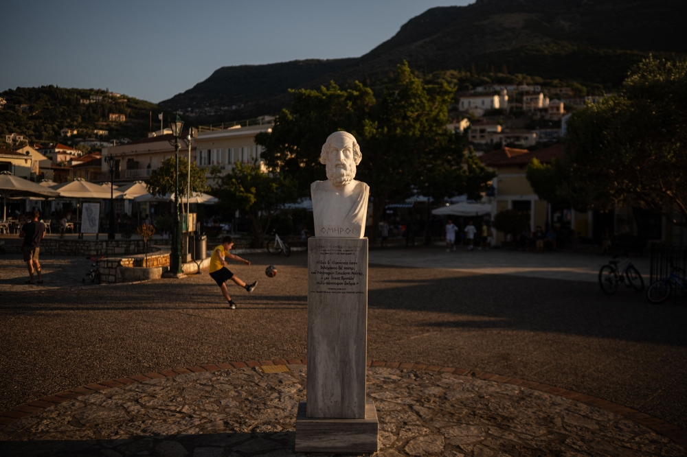 A child plays football next to a marble bust of ancient Greek poet Homer in the central square of Vathy, on the island of Ithaca, in the Ionian Sea, on August 3, 2026. Ithaca, the home to the hero Odysseus in Homer's Odyssey, is far from Greece's main tourist hubs it has never been a regular stop for travellers. The release of the blockbuster film The Odyssey has the island's businesses and officials expecting a rise touristic activity. — AFP pic