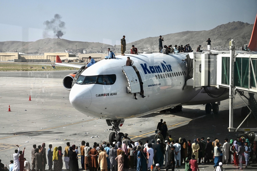This file picture shows Afghan people climb atop a plane as they wait at the Kabul airport in Kabul on August 16, 2021, as thousands of people mobbed the city’s airport trying to flee the Taliban. — AFP pic