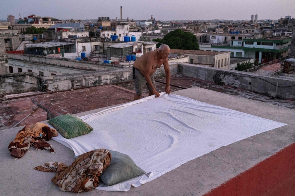 Alexis Miranda spreads a sheet over the rooftop of a residential building at sunset in Old Havana on August 11, 2026. — AFP pic