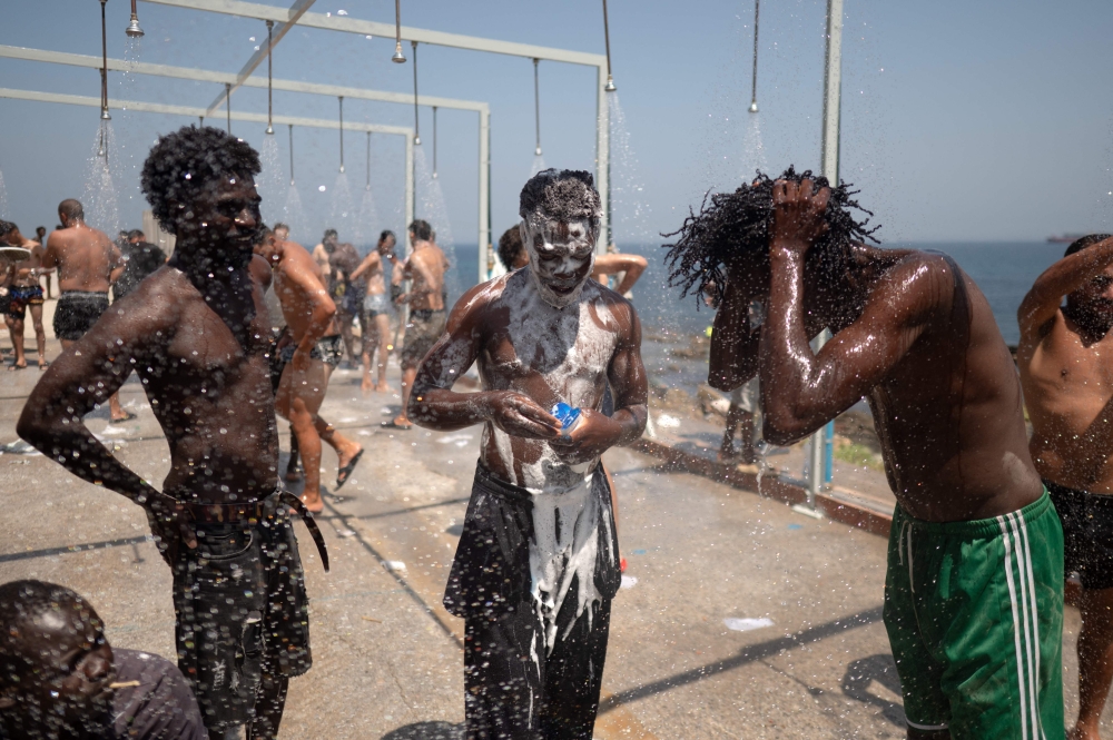 Migrants take a shower after swimming across to the Spanish enclave of Ceuta in North Africa on August 15, 2026. — AFP pic