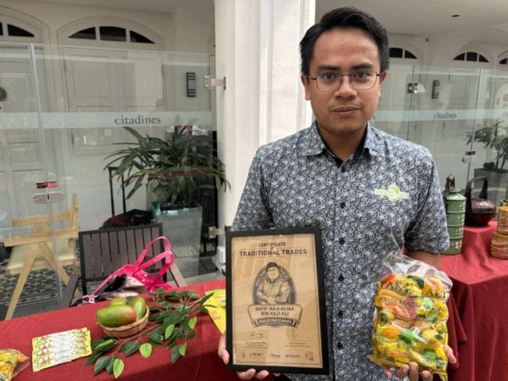 Jeruk Madu Pak Ali’s marketing and public relations executive Mohd Shahrul Nizam Shahidin showing the packaged pickled fruits and the traditional trades certificate from Penang Global Tourism. — Picture by Opalyn Mok