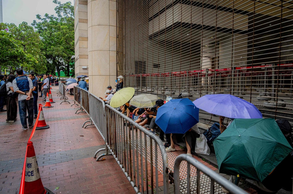 People wait under umbrellas outside the West Kowloon Magistrates’ Courts ahead of the verdict in the national security trial of two pro-democracy Tiananmen activists, in Hong Kong August 21, 2026. — AFP pic