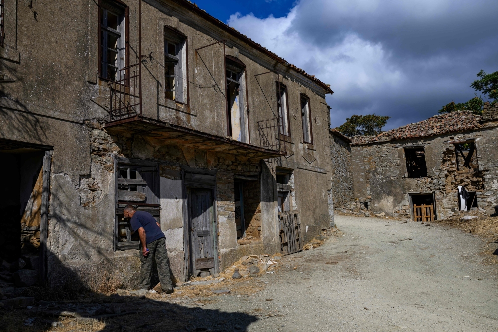 Local resident Yorgi Baki looks through a window of an abandoned house in Derekoy, a village largely deserted by Greeks after 1960s clashes. — AFP pic