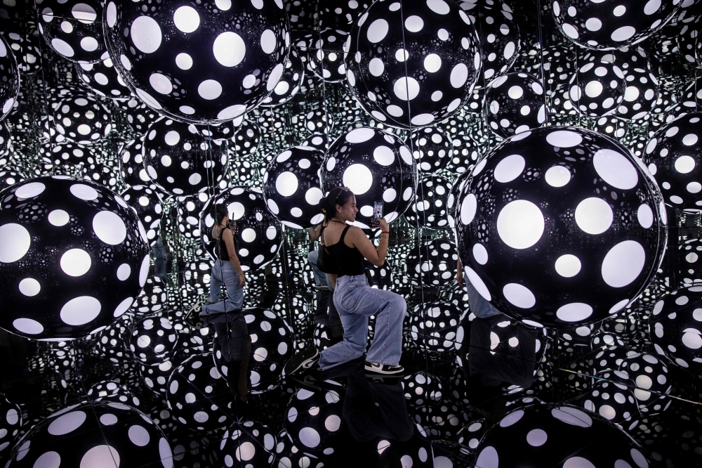 A woman takes photos at Yayoi Kusama’s ‘Dots Obsession – Aspiring to Heaven’s Love’ installation in Hong Kong on August 4, 2023. — AFP pic