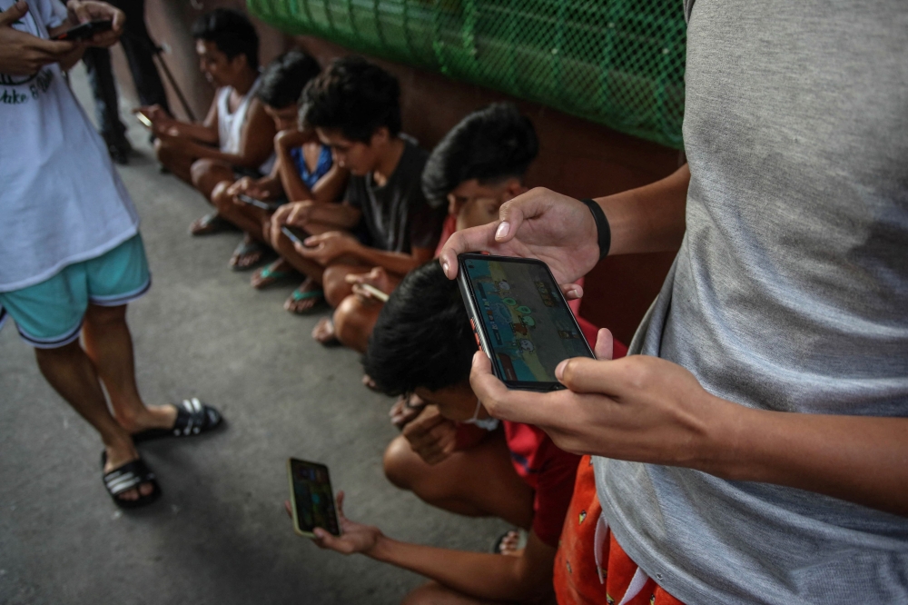 Youngsters use their mobile phones in a neighbourhood alley in Malabon, suburban Manila on December 15, 2021. — AFP pic
