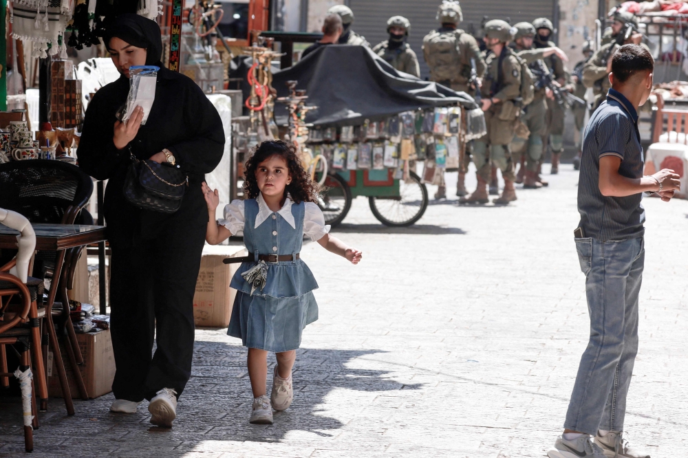 A Palestinian youth (right) watches armed Israeli soldiers patrol on foot through a market in Nablus’s Old City in the northern Israeli-occupied West Bank on August 9, 2026. — AFP pic