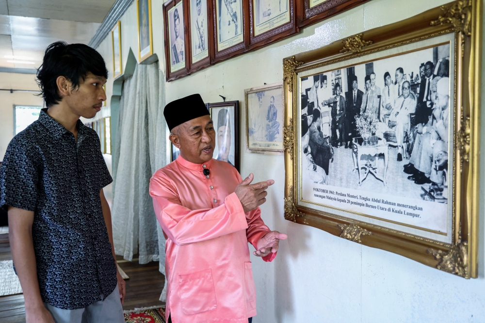 Homeowner Mohd Halikin Angga (right) recounts the formation of the Federation of Malaysia to his son, Muhammad Mahathir Mohd Halikin, at their residence, which is decorated in the colours of the Jalur Gemilang. The living room is adorned with official portraits of the Yang di‑Pertuan Agong, the Yang di‑Pertua Negeri Sabah and Malaysia’s prime ministers, from Tunku Abdul Rahman Putra Al‑Haj to the current leadership. Among his most treasured items is a historic photograph of Tunku Abdul Rahman meeting 20 North Borneo leaders in 1961 to discuss the formation of Malaysia. — Bernama pic