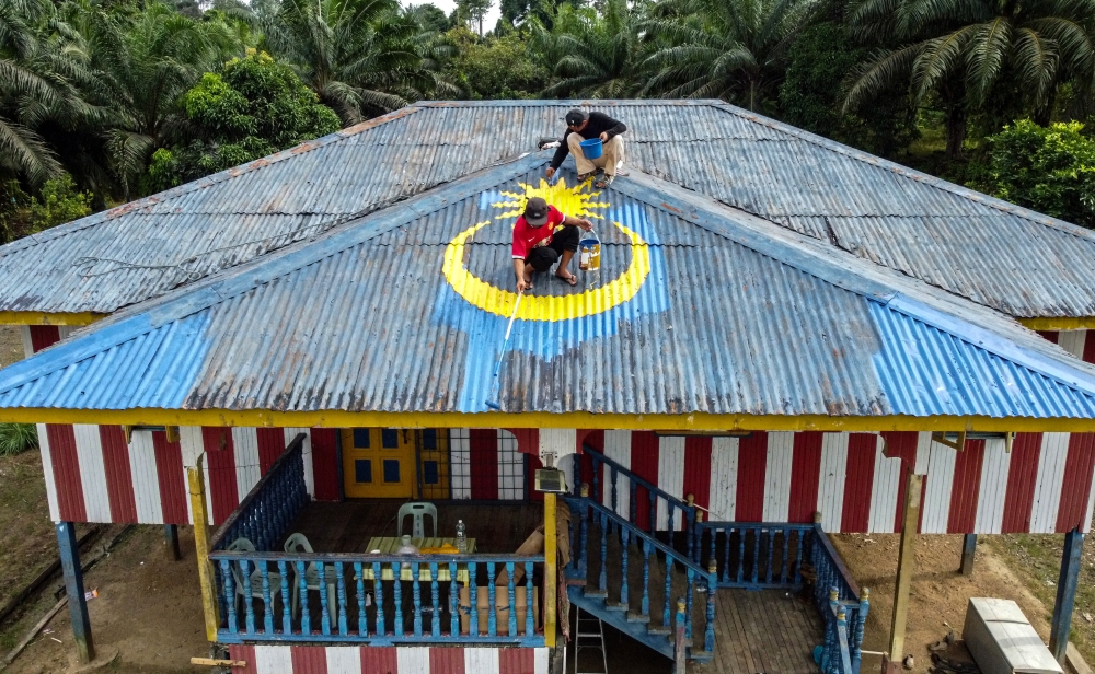Workers paint the roof of Mohd Halikin Angga’s home in the colours and motifs of the Jalur Gemilang. — Bernama pic