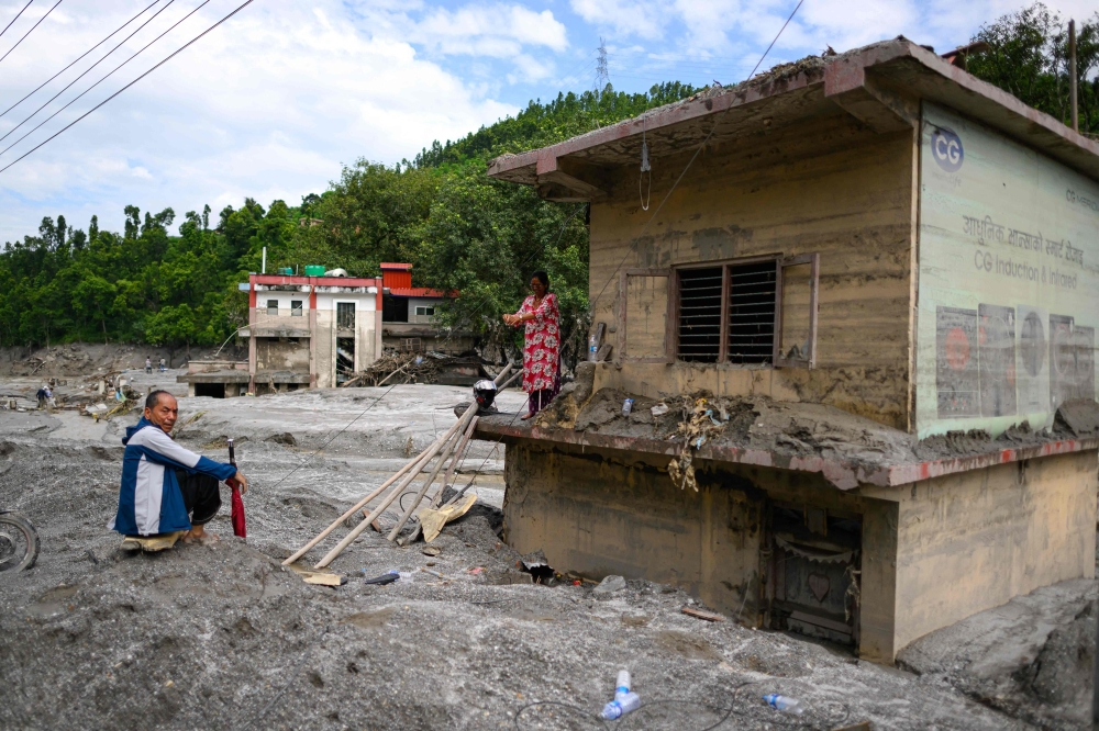 A woman (right) stands atop her house covered in mud in the aftermath of flash floods at Baireni in Nepal's Dhading district on August 30, 2026. The number of people missing in the catastrophic flood that sliced through the border area between Nepal and Tibet exceeded 3,000 on August 30, as rescuers scoured deep, leg-sucking mud for survivors. — AFP pic