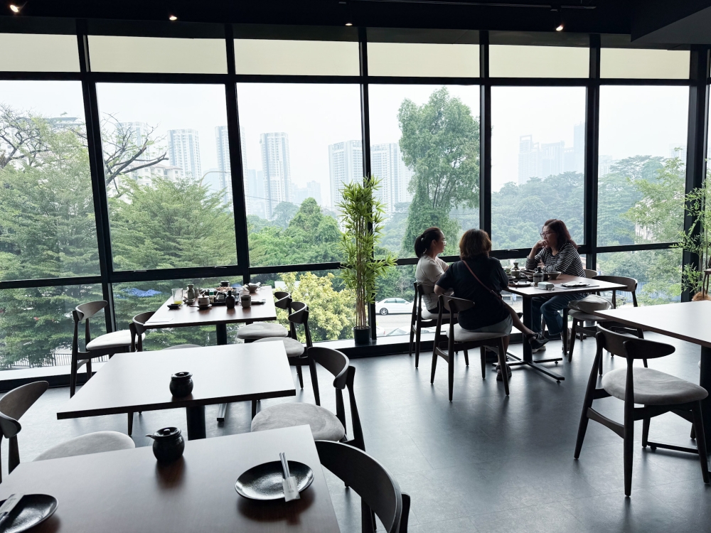 The dining area feels vast with floor-to-ceiling windows offering a view of Taman Desa. 