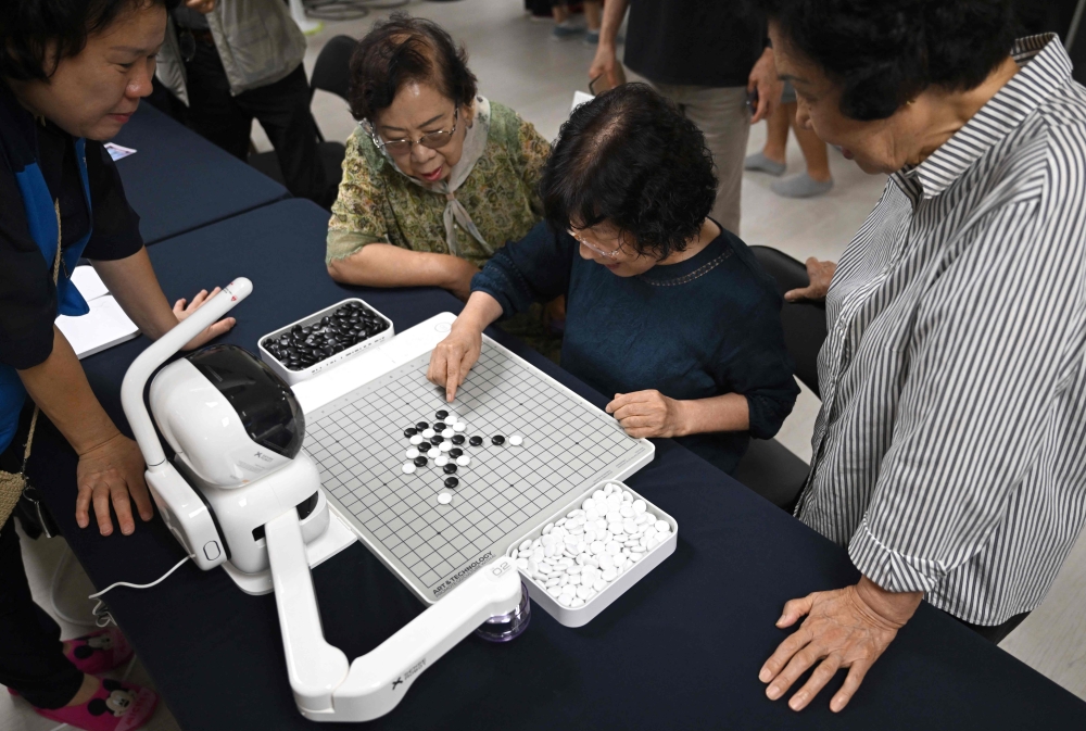 This picture taken on August 13, 2026 shows elderly people playing a game of Gomoku, also called five in a row, with a robot during a government-organised digital survival training at a senior community centre in Suwon. Age gaps in digital literacy are a global concern, yet the gulf has widened massively in the hyper-connected and fast-aging country, prompting national campaigns to bridge it. — AFP pic