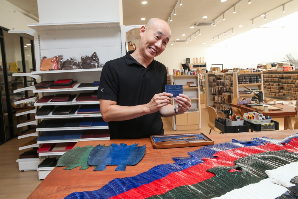 Alec is seen here at Kelang Leather’s former Zebra Square outlet with a cardholder he made, with crocodile skin in the foreground, and with the two smaller pieces of leather on the table made from monitor lizard skin. — Picture by Choo Choy May
