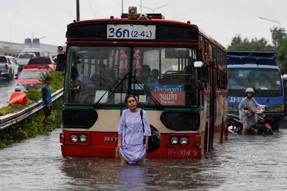 A woman walks through flood waters in front of a bus after heavy rain in Bangkok on September 26, 2026. — AFP pic