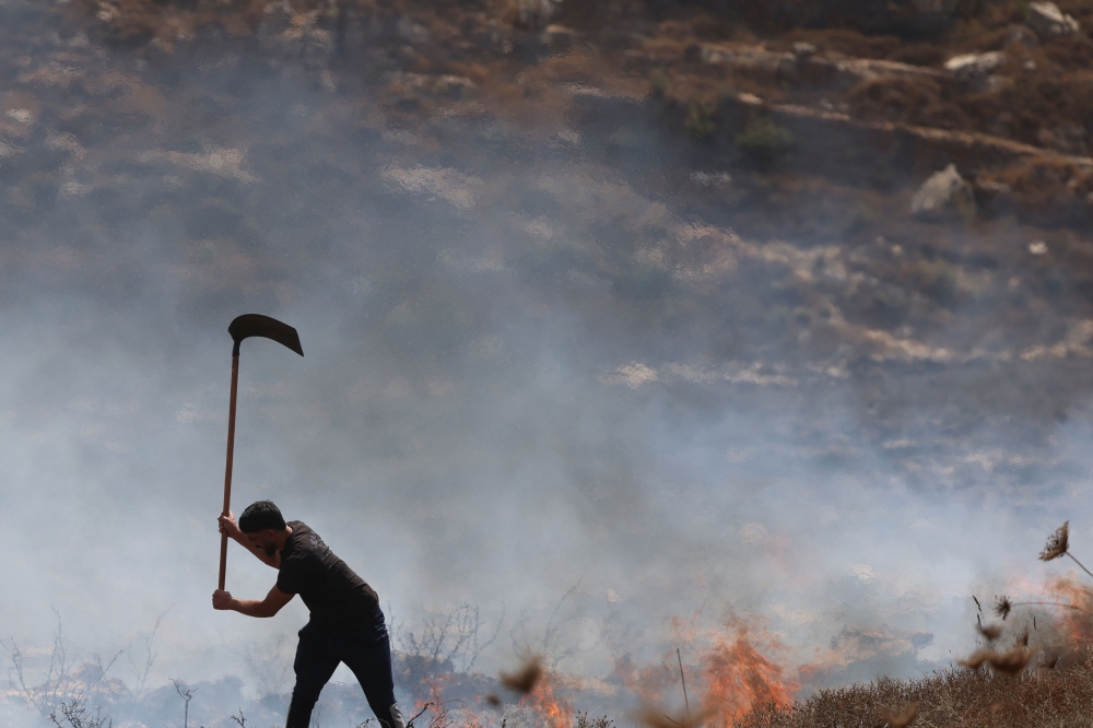 A local Palestinian farmer tries to extinguish fires on land after Israel’s army soldiers fired tear gas as they harvested their olives, resulting in the dry fields catching fire, in the village of Asira al-Qibliya, south of the Israeli-occupied city of Nablus, on October 3, 2026. — AFP pic