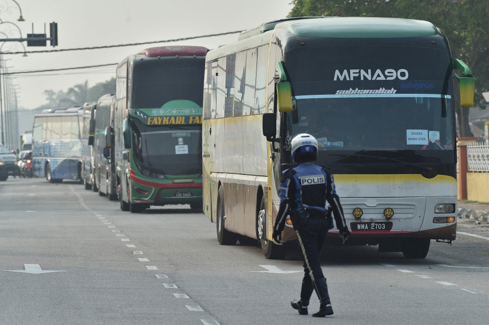 A policeman walks in front of buses carrying Myanmar nationals being repatriated from Malaysia to their homeland, seen heading toward the naval base in Lumut, on the outskirts of Kuala Lumpur September 29, 2026. — AFP pic