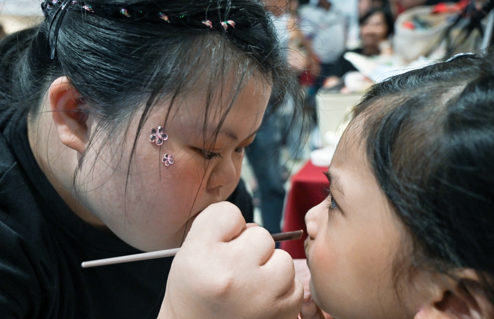 Special needs makeup artist Loh Xin Jeanne, 19, (left) applies makeup to a child, October 4, 2026. — Bernama pic 