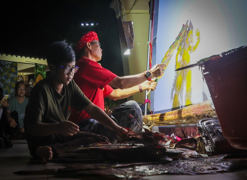 At a ‘wayang kulit’ performance in Tok Bali, Nik Imanuddin Hadeef Nik Izdiharuddin, 10 (second right), learns from and assists Sri Cindayu ‘Wayang Kulit’ Association founder Kang Boon Ann, 58. — Bernama pic