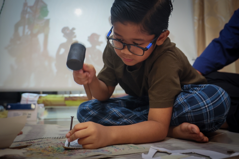Nik Imanuddin Hadeef Nik Izdiharuddin, 10, focuses on making a ‘wayang kulit’ puppet, one of several skills he is learning alongside puppeteering and playing traditional musical instruments. — Bernama pic