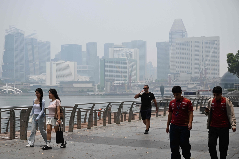 People walk along the boulevard at Marina Bay as buildings are seen shrouded with haze in Singapore on October 6, 2026. — AFP pic