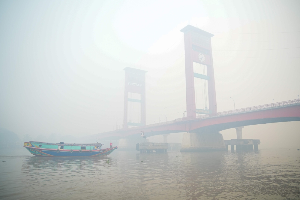 A traditional passenger boat navigates the Musi River in Palembang, South Sumatra on October 5, 2026, as haze from forest and land fires in the region blankets the sky and surrounding areas. — AFP pic