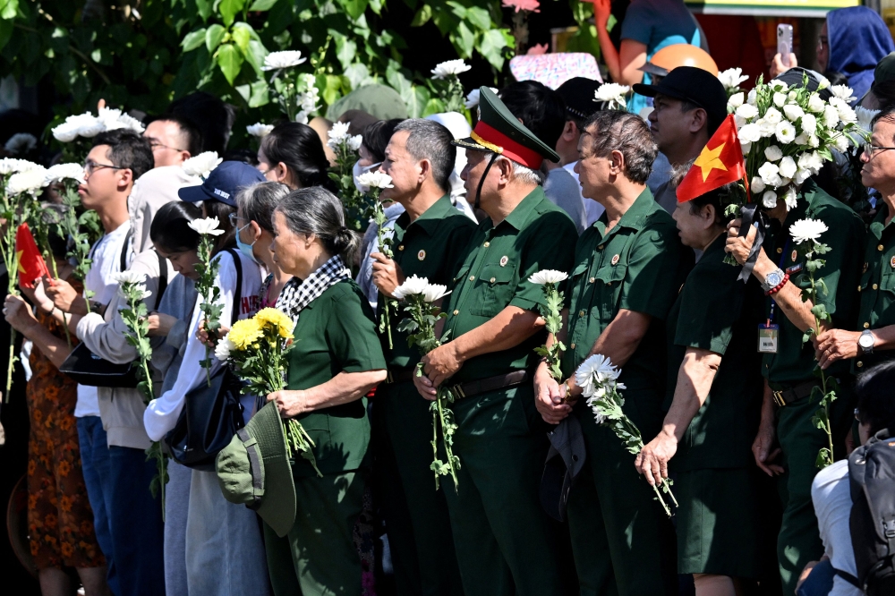 People gather with flowers by a roadside as they wait for the vehicle transporting the remains of fallen soldiers to pass by in Ho Chi Minh City October 14, 2026. — AFP pic