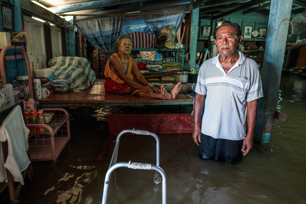 Thai retiree Somjit Kitklin, 93 (centre), sits on a raised metal‑and‑wood platform as her son Sommai Kitklin, 63, stands in floodwater inside their home in Sena district, Ayutthaya province, October 7, 2026. — AFP pic