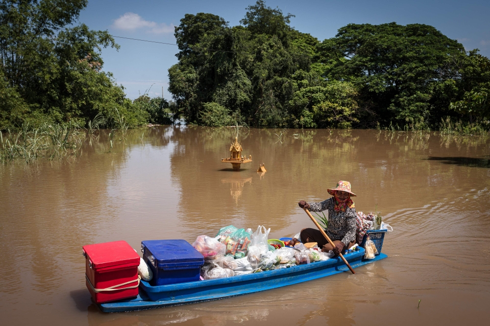 A vendor sells prepared food from her boat as she paddles past a flooded shrine in Sena district in the central Thai province of Ayutthaya on October 7.
