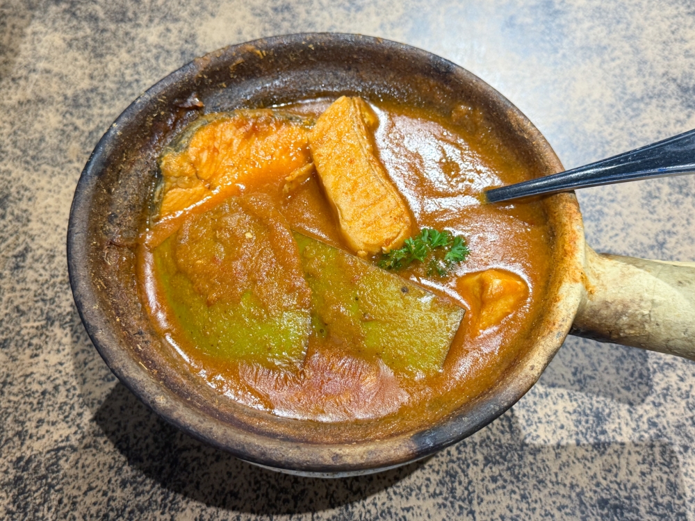 Salmon Mango Curry is kept warm in a small claypot; it has a thick curry with tangy mango pulp and a piece of salmon. — Picture by Lee Khang Yi