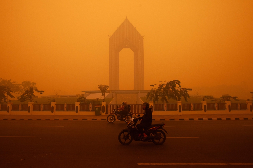 Motorcyclists ride in the morning in Palangkaraya, Central Kalimantan on October 14, 2026, amid thick haze from forest and land fires in the region. — AFP pic
