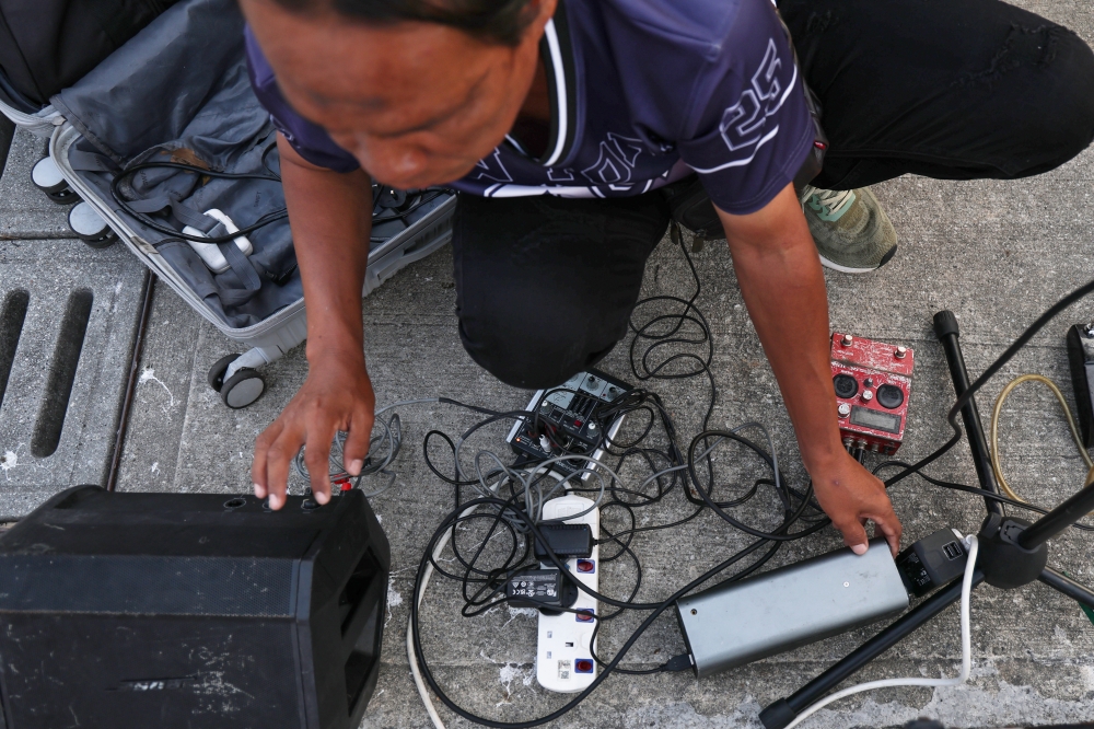 Rodie Jainahum sets up his musical equipment before a performance in Bangsar. He said transporting more than 150kg of gear by e-hailing services significantly cuts into his earnings. — Bernama pic