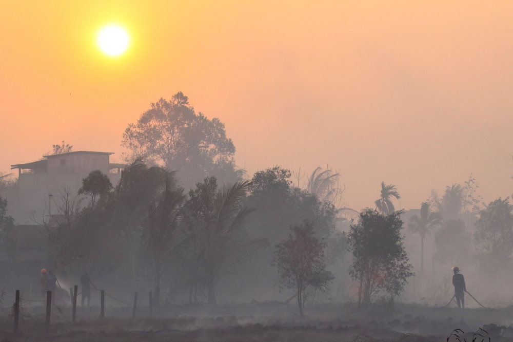 Firefighters and residents use hoses to extinguish spreading wildfires amid dense smoke and a hazy sunset in Banjarbaru, South Kalimantan province on October 21, 2026. — AFP pic